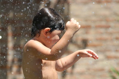 Shirtless boy playing with water while standing outdoors