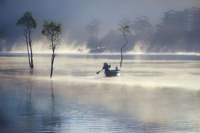 Rear view of person rowing boat in lake during foggy weather