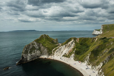 Mossy mountains by sea against cloudy sky at durdle door