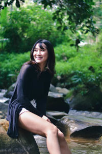 Portrait of young woman sitting on rock by lake