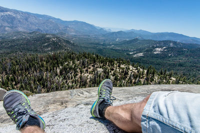 Low section of man sitting on mountain against sky