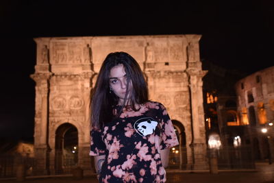 Portrait of woman standing against illuminated building at night