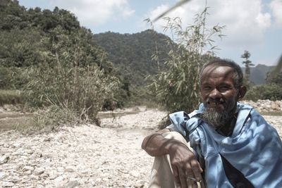 Portrait of smiling man siting against mountain and sky