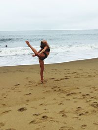 Full length of young woman exercising at beach against sky