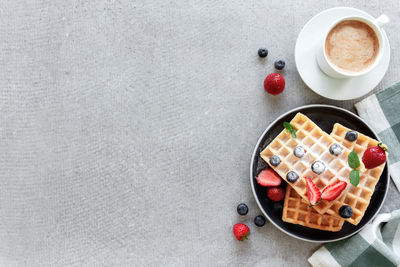 Stack of sugar powdered waffles with honey on a plate on the towel and gray concrete or slate table