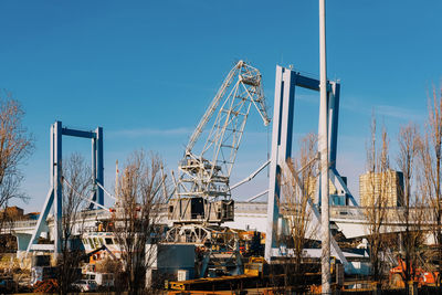 Low angle view of cranes at pier against blue sky