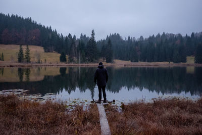 Rear view of man standing by lake against sky