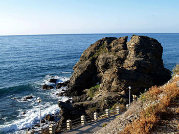 Rock formation by sea against clear sky