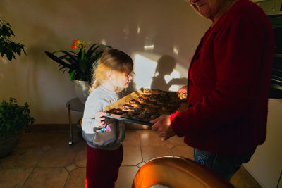 Midsection of grandmother holding cookies in tray while standing with granddaughter at home