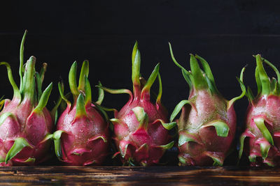 Close-up of wet pitayas on wooden table against black background