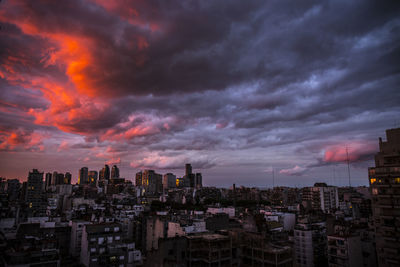 Buildings in city against dramatic sky during sunset