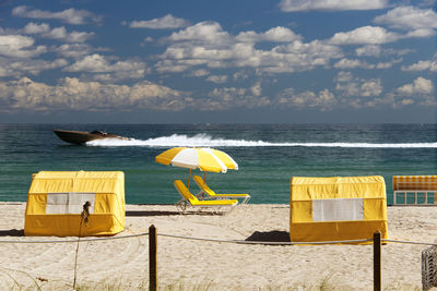 Yellow deck chairs on beach against sky