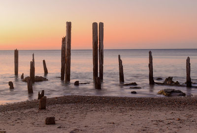 Wooden posts on beach against sky during sunset