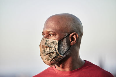 Bald man wearing protective face mask at rooftop against sky during pandemic