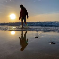 Rear view of man standing on beach during sunset