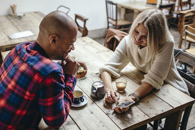 Multi-ethnic couple using mobile phone at table in coffee shop