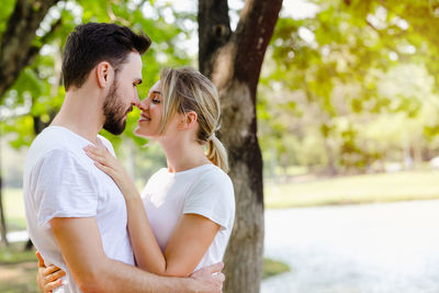 Side view of young couple standing against trees