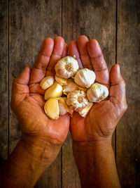 Cropped hands holding garlic over hardwood floor