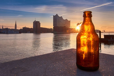 Bottle at riverbank in city during sunset