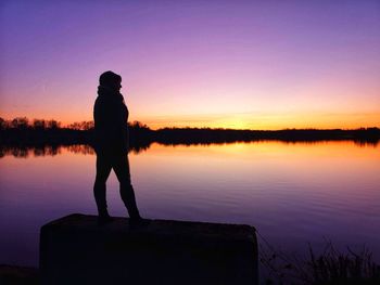 Silhouette man standing by lake against sky during sunset