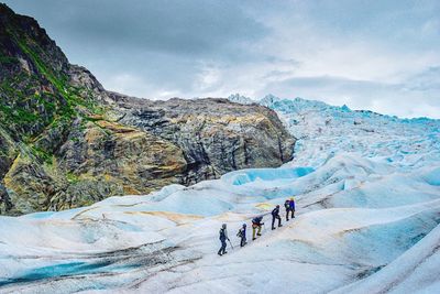 High angle view of people hiking on snow covered mountains against sky