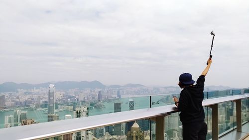 Rear view of man standing by railing in city against sky