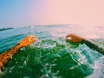 Cropped hand of man in sea against sky during sunset