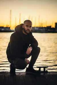 Man sitting on pier against sky during sunset