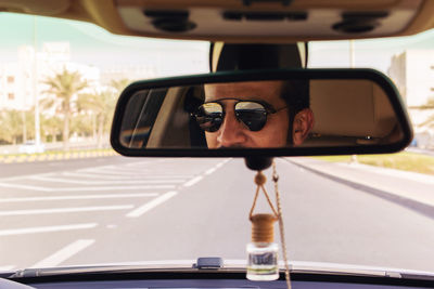 Man reflecting on rear-view mirror in car