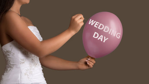 Midsection of bride holding balloon and needle against gray background