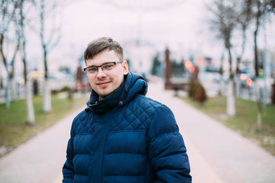 Portrait of smiling man standing on footpath against sky