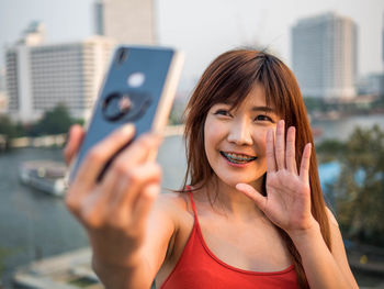 Portrait of smiling young woman using mobile phone in city