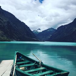 Boat moored by pier on lake against cloudy sky