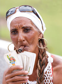 Portrait of woman holding playing cards and smoking cigar while sitting outdoors