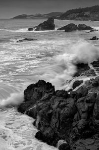 Black and white image of waves crashing on rock formations