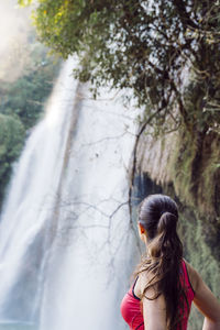 Side view of woman looking at waterfall in forest