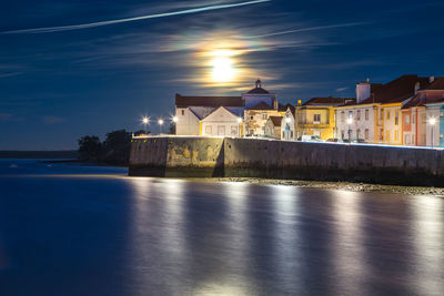 Illuminated cityscape by sea against sky at night