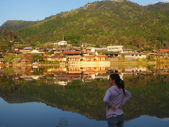 Rear view of woman standing by lake against building