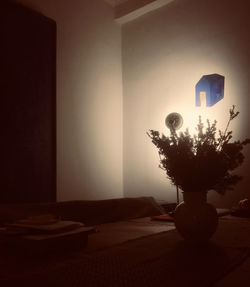 Illuminated lamp on table against wall at home