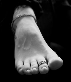 Low section of woman wearing anklet against black background