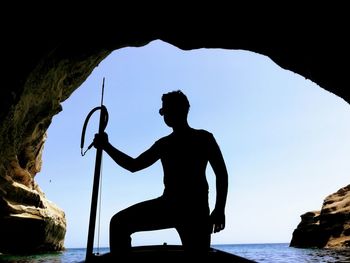 Silhouette man standing on rock by sea against clear sky