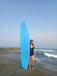 Full length on woman with surfboard standing on beach against clear sky