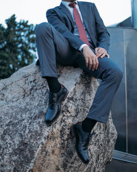 Low section of businessman sitting on rock formation