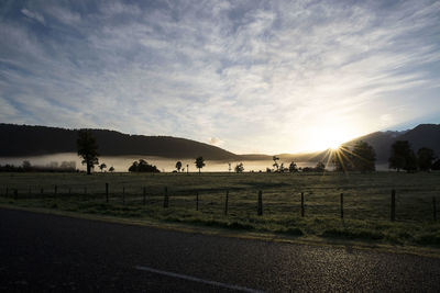 Road by field against sky during sunset