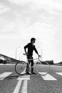Side view of man with bicycle standing on road against sky