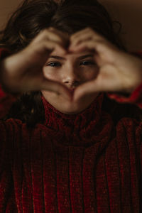 Close-up portrait of girl making heart shape against brown background