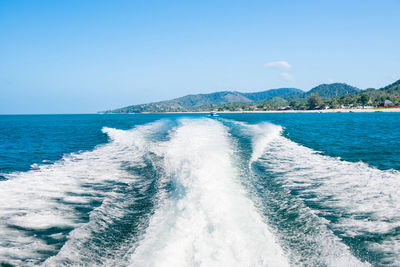 Wave from cruise boat on water surface and horizon with blue sea and island coast at background