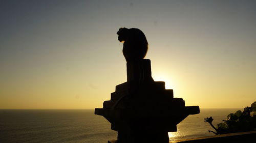 Silhouette statue by sea against clear sky during sunset