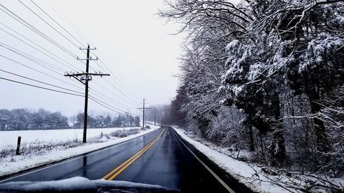 Snow covered road by trees against clear sky