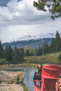 Woman sitting by lake against mountain range